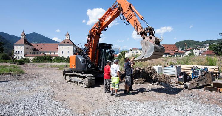 Ein Bagger auf der Baustelle im Hofburggarten; daneben stehen zwei Arbeiter.